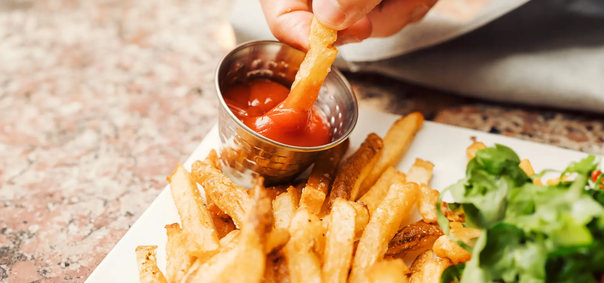 Zwei Finger dippen einen Pommes in den Ketchup