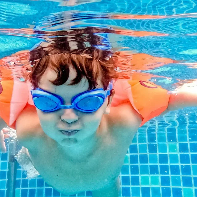Junge mit Taucherbrille und Schwimmflügeln taucht unter Wasser