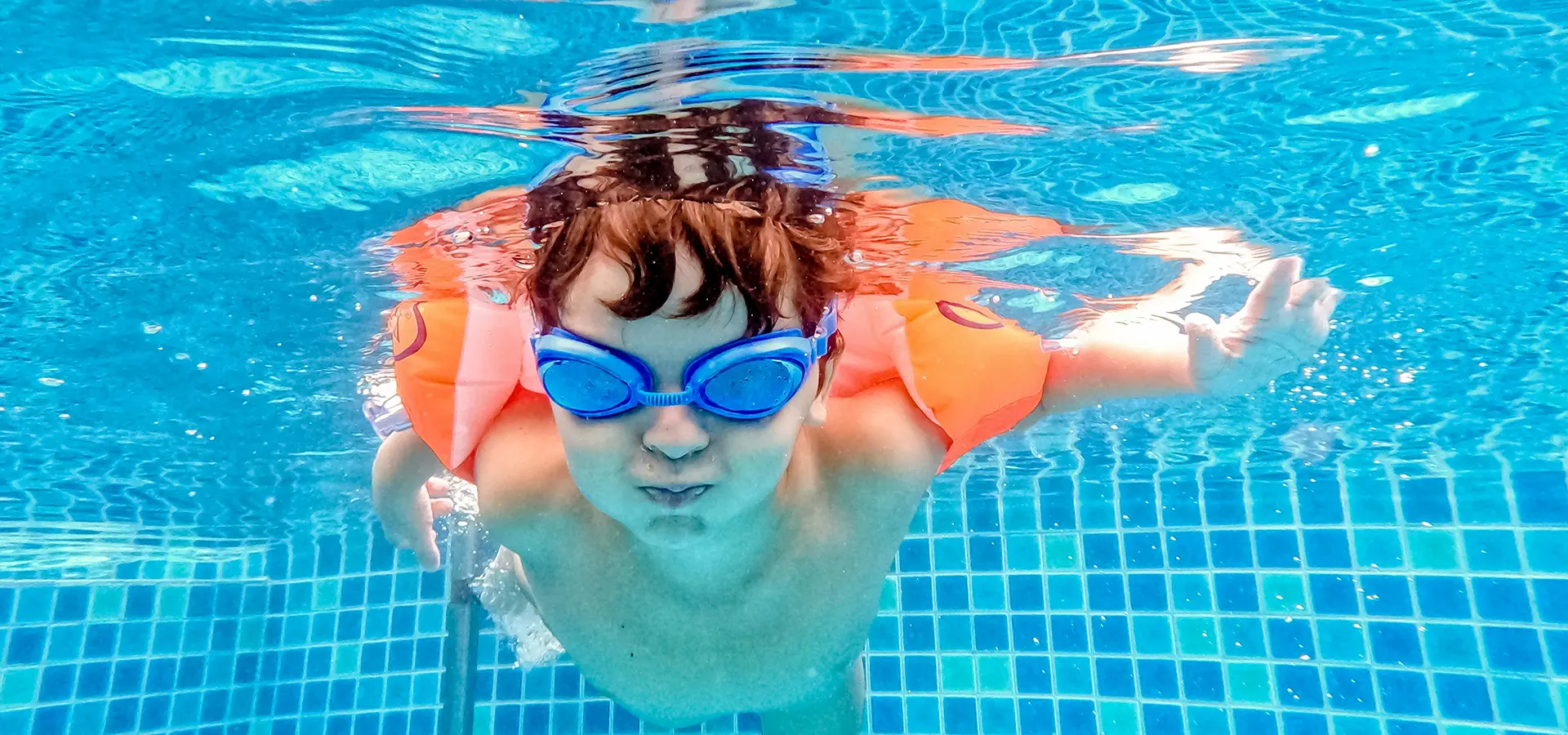 Junge mit Taucherbrille und Schwimmflügeln taucht unter Wasser